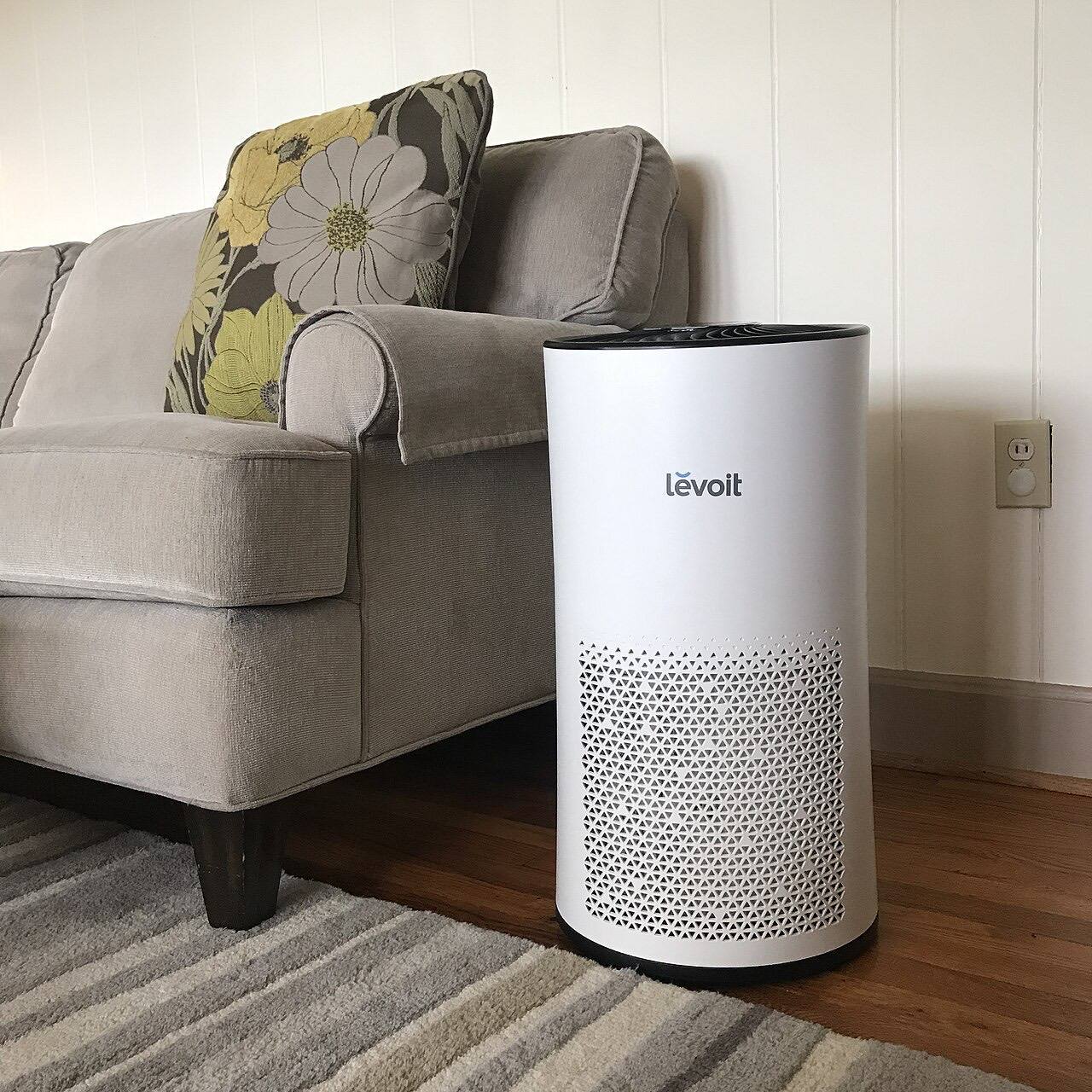 An air purifier in a living room next to a couch. Brand: Levoit LV-H133 If used, please credit us by using the following link: https://homeairguides.com