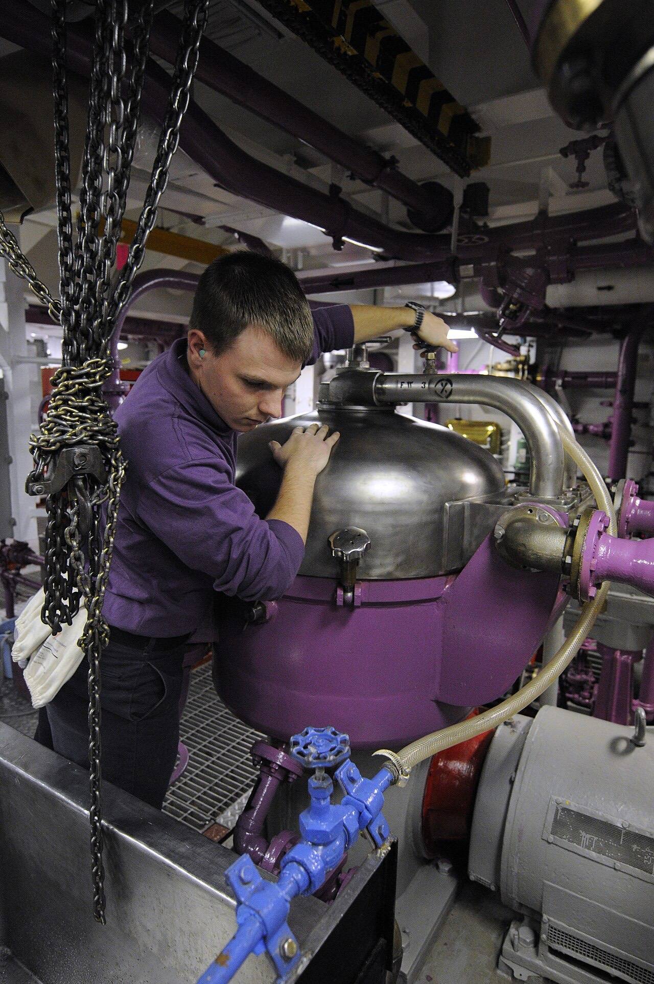 US Navy 101218-N-8040H-001 Aviation Boatswain's Mate (Fuel) Airman Apprentice Cody Turner turns an inlet valve to ensure a purifier is operating pr